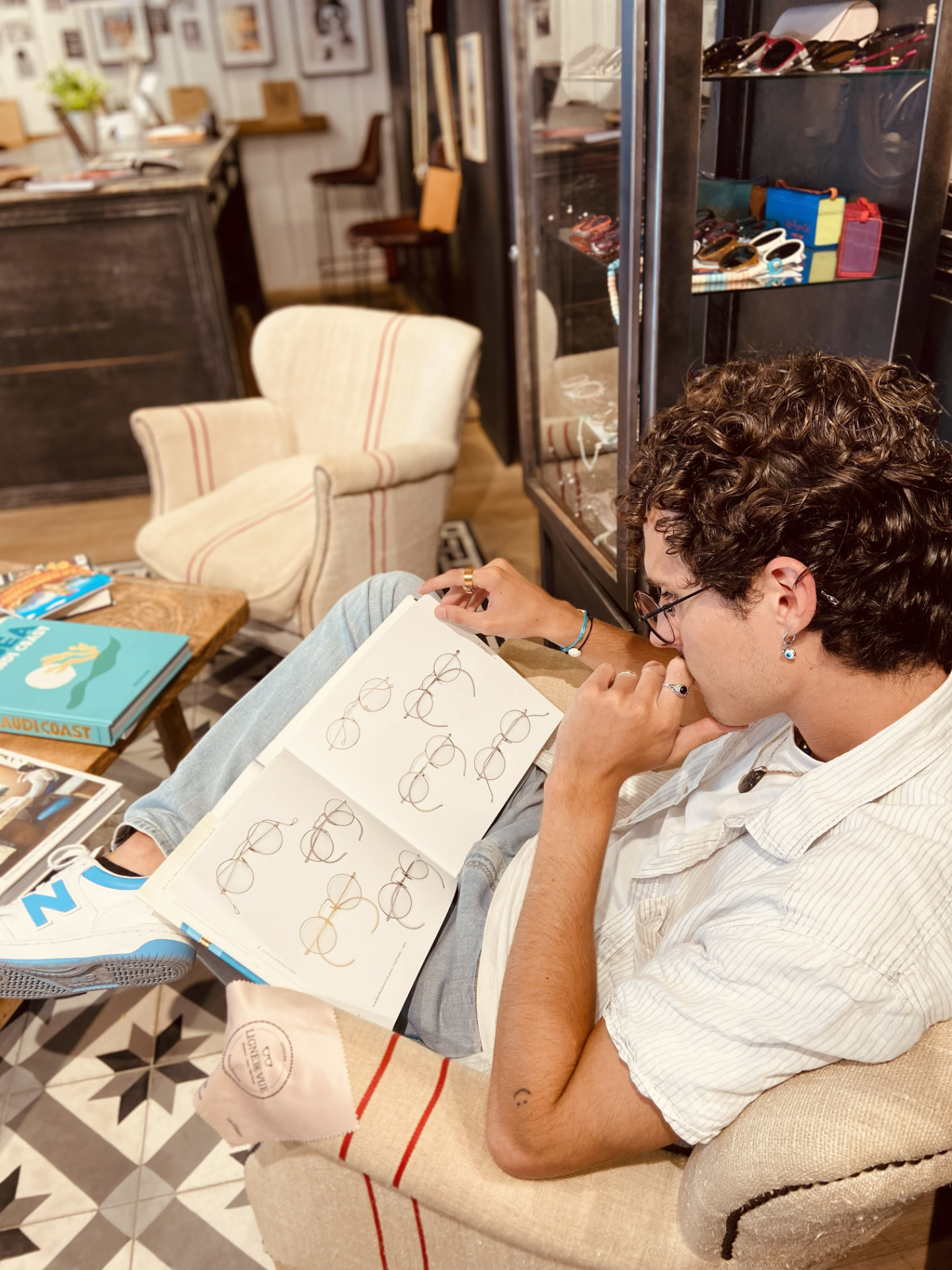 Couli assis dans une boutique de lunettes, feuilletant un carnet de croquis de montures