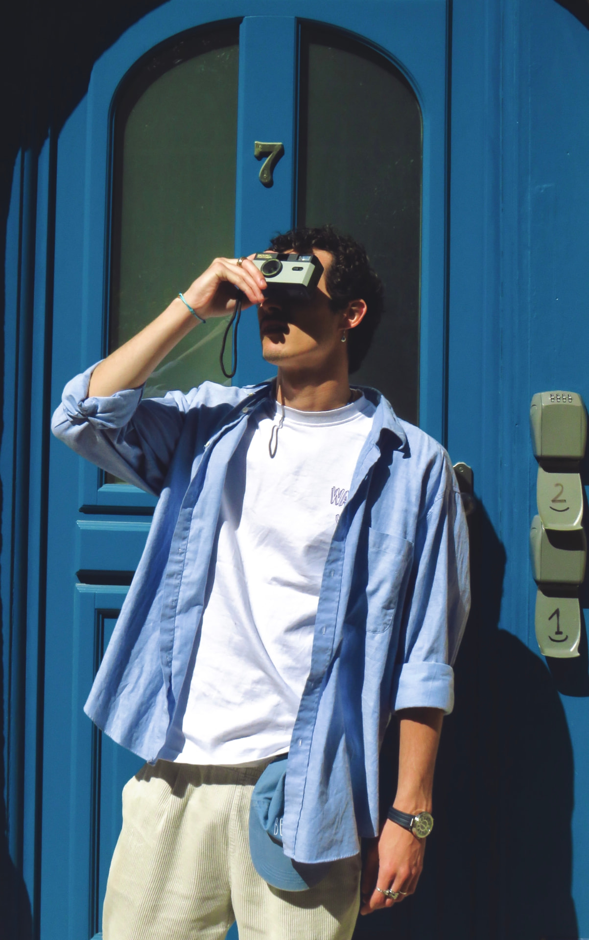 Couli devant une porte bleue, prenant une photo avec un appareil argentique